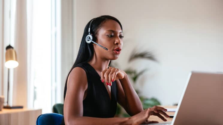 Young elegant African American female in headset having call while looking at screen of laptop