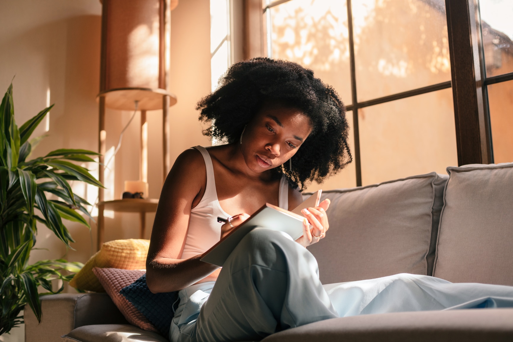 Young black woman at home, sitting on the couch and writing in her notebook.