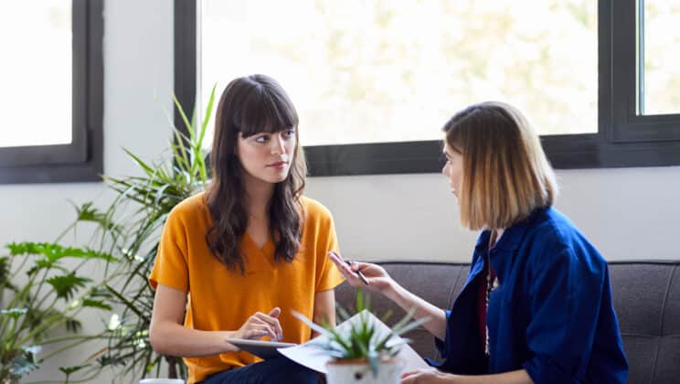 Businesswomen discussing while sitting on sofa against window at creative office